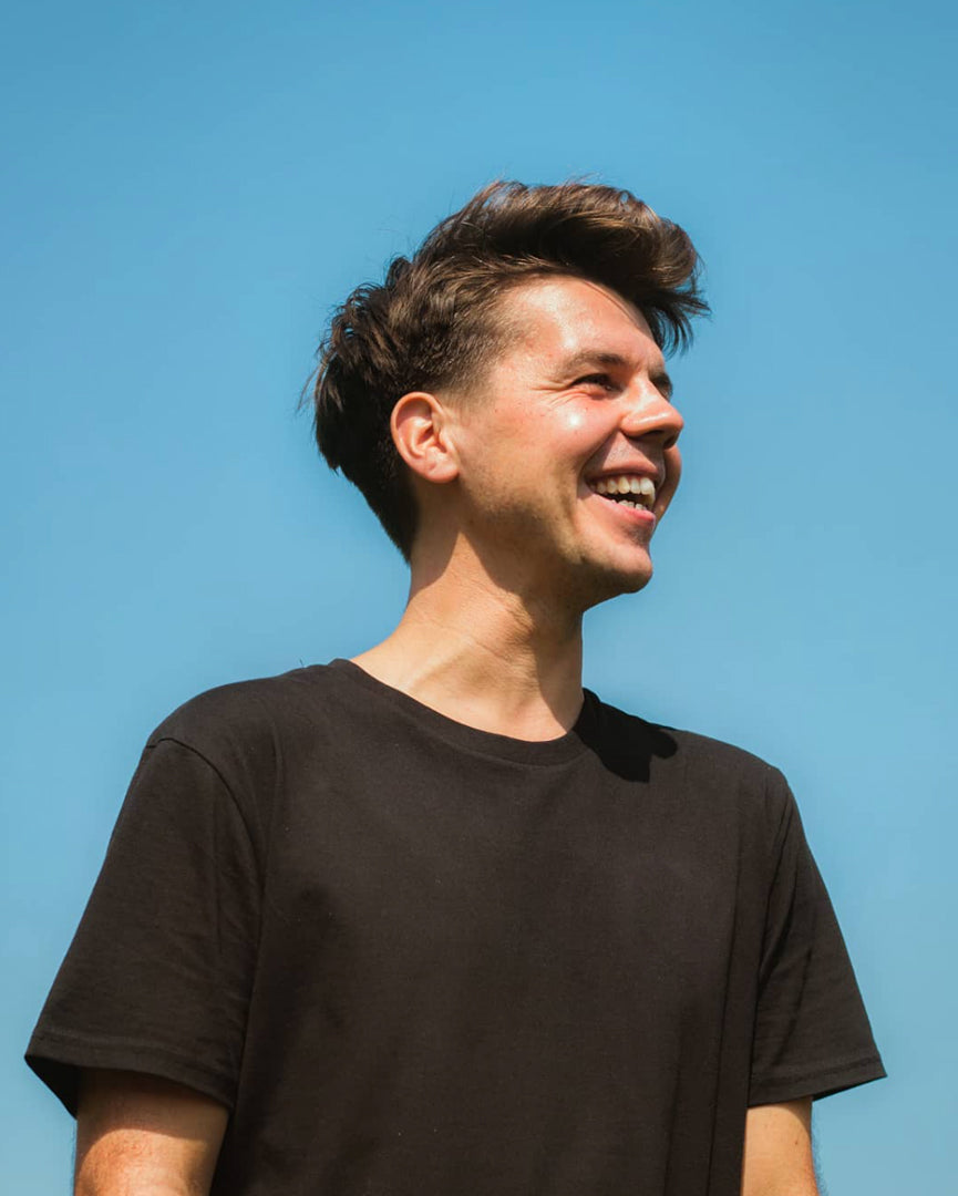 Man smiling against a blue sky wearing a black organic cotton t-shirt from sustainable clothing brand Goose Studios