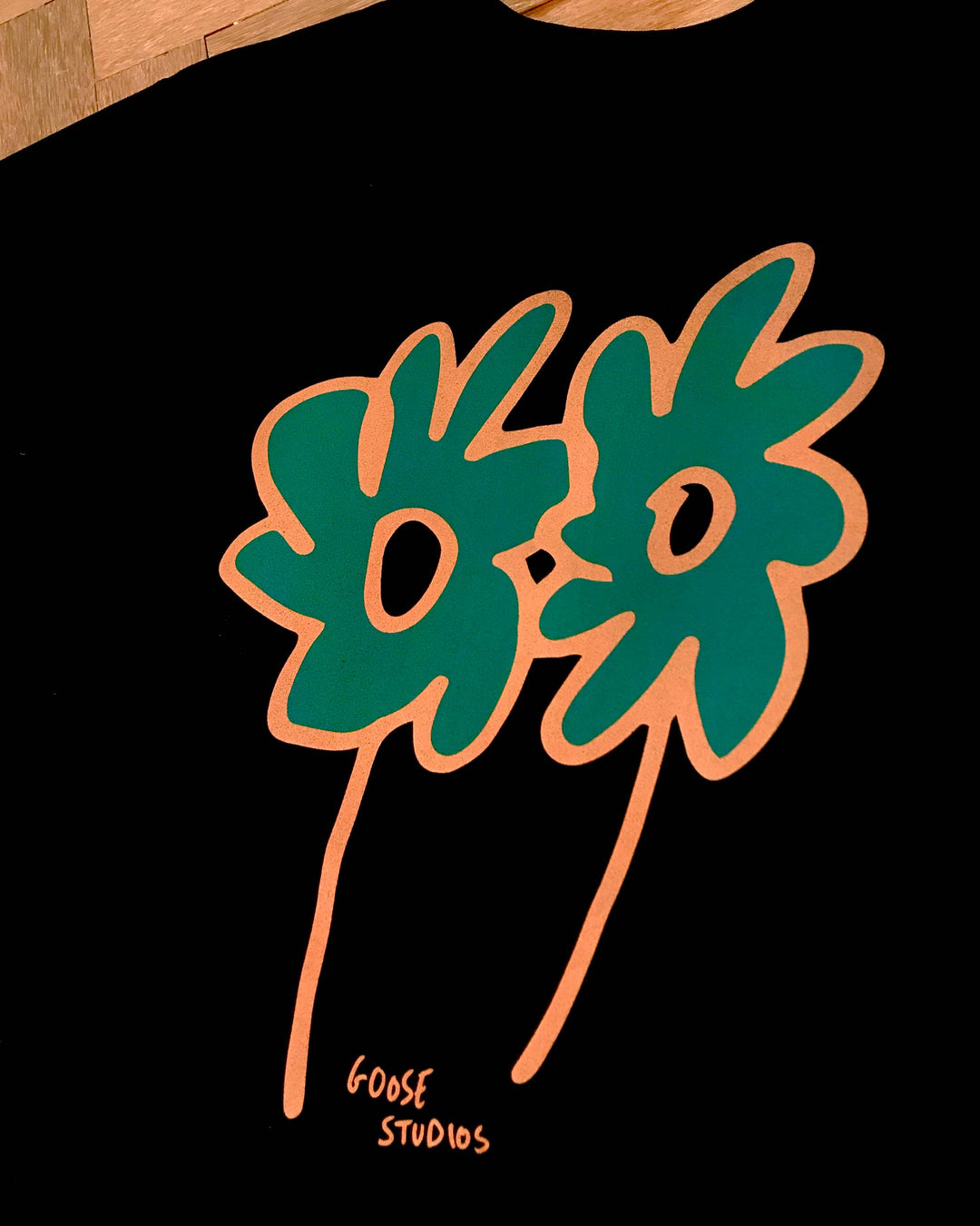 Two stylized flowers in orange and green printed on a black 240gsm t-shirt, featuring the text &