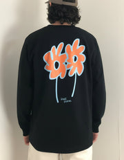 Person wearing a black organic cotton long-sleeve shirt with colorful flower designs on the back, standing indoors.