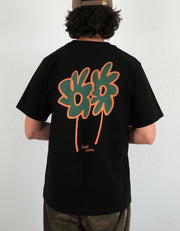Man wearing a black heavyweight organic cotton t-shirt with a colourful flower design on the back, standing indoors.