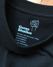 Black t-shirt with 'Goose Studios' branding and text on the collar, stating the style is made from 100% organic cotton - 240gsm