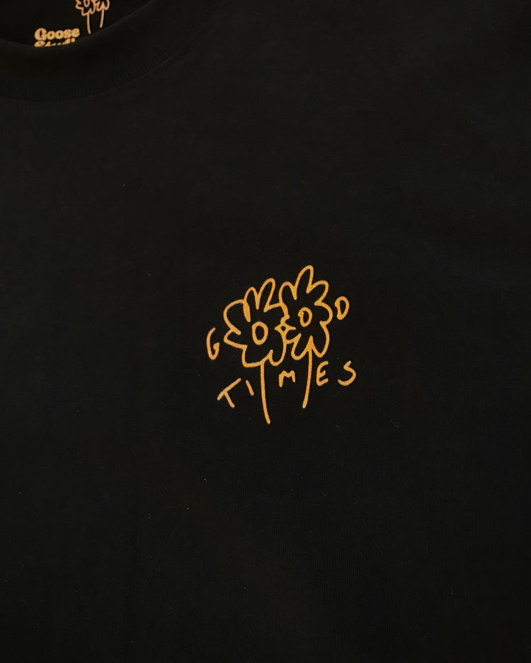Black t-shirt with an orange hand drawn logo featuring the Goose Studios flowers with the words Good Times incorporated intro the design, printed on a black heavyweight organic cotton t-shirt.