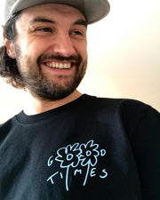 Man wearing a black organic cotton long-sleeve tee with a blue flower design and text, smiling.