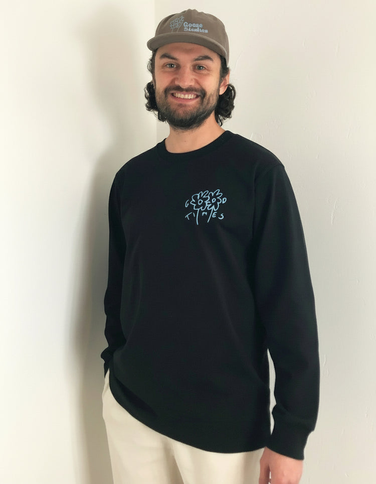 Man wearing a black long sleeve organic cotton t-shirt from Goose Studios with a logo and a cap, standing indoors.