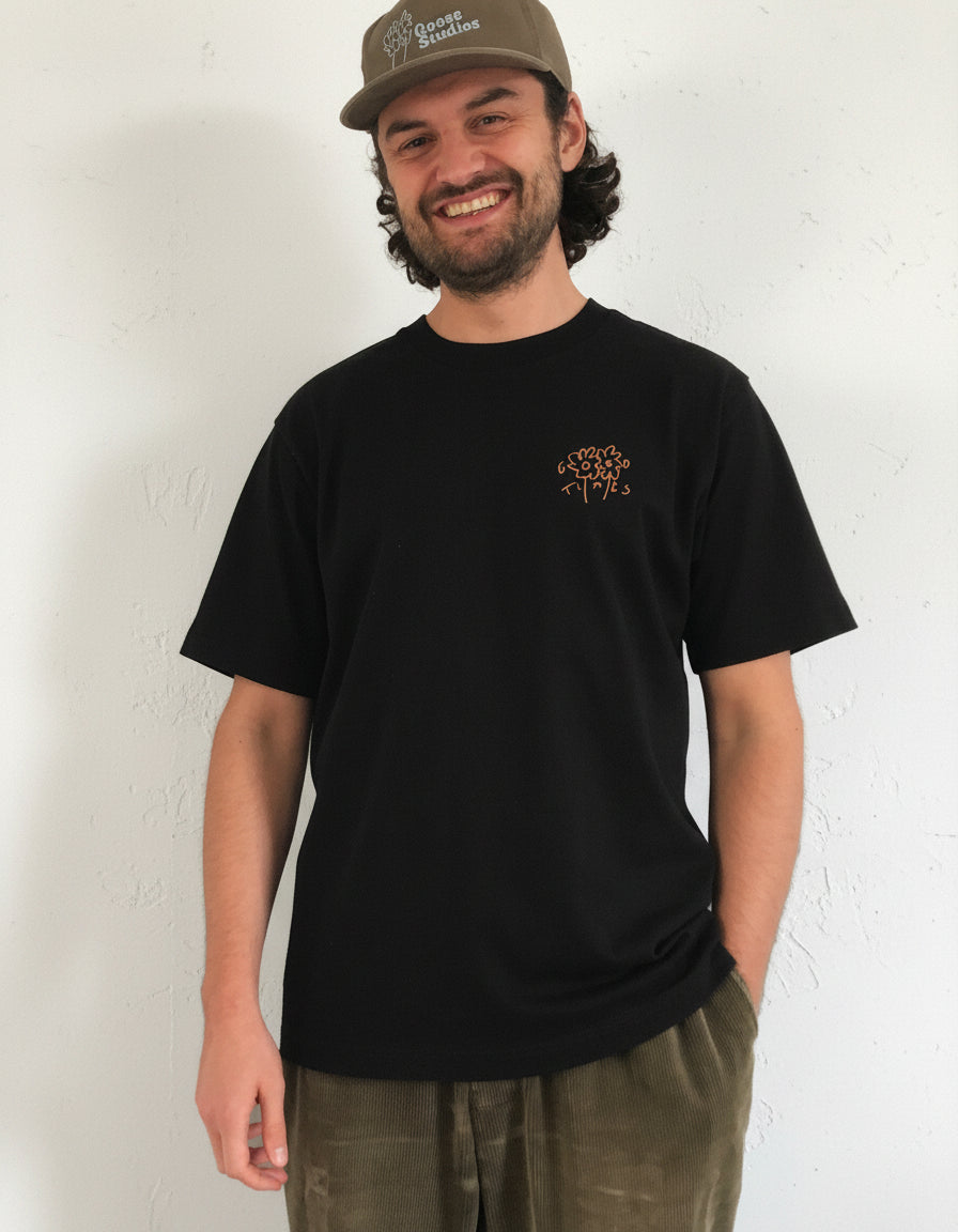 Man wearing a black 240gsm organic cotton t-shirt with a Good Times logo and a cap on a white background