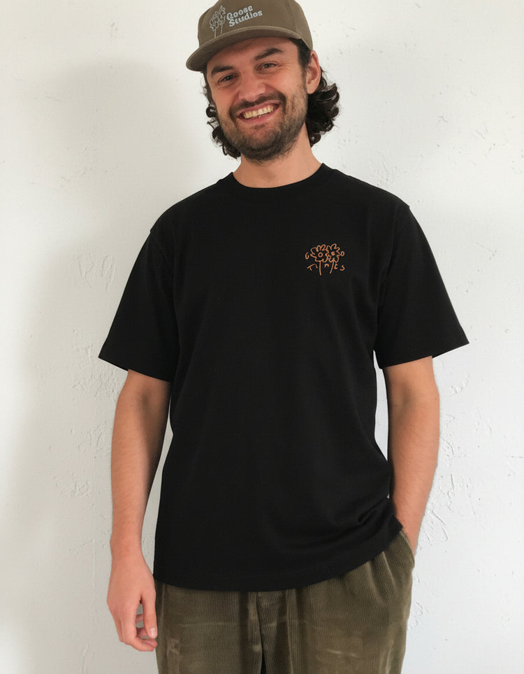 Man wearing a black 240gsm organic cotton t-shirt with a Good Times logo and a cap on a white background