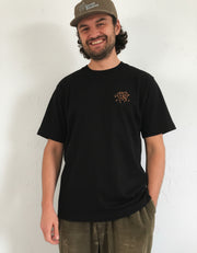 Man wearing a black 240gsm organic cotton t-shirt with a Good Times logo and a cap on a white background