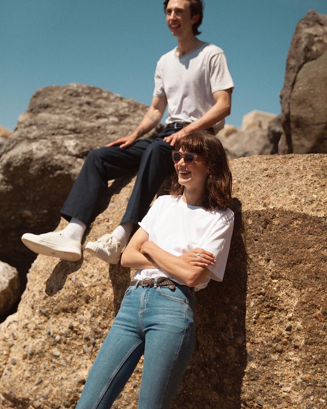 Man and woman sitting on rocks in the sun wearing organic cotton t-shirts from sustainable clothing brand Goose Studios.