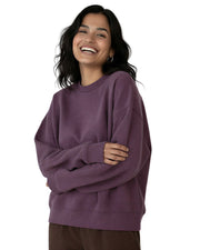 Woman standing with her arms crossed wearing a purple organic cotton sweatshirt from Goose Studios and brown trousers