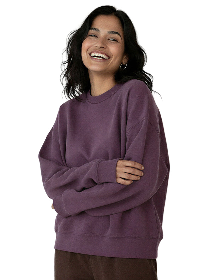 Woman standing with her arms crossed wearing a purple organic cotton sweatshirt from Goose Studios and brown trousers