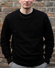 Man standing, wearing a black organic cotton sweatshirt from Goose Studios, a sustainable clothing brand from the UK