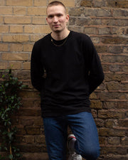 Man standing wearing black organic cotton long sleeve t-shirt with blue jeans.