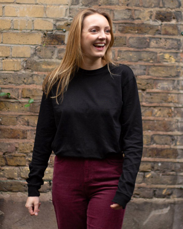 Woman standing wearing men's black organic cotton long sleeve t-shirt.