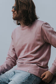 Man sitting, wearing a brushed back organic cotton sweatshirt with crew neck, in pastel pink, from sustainable clothing brand Goose Studios