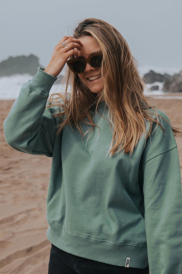 Woman on a beach wearing organic cotton sweatshirt with a drop shoulder from Goose Studios sustainable clothing